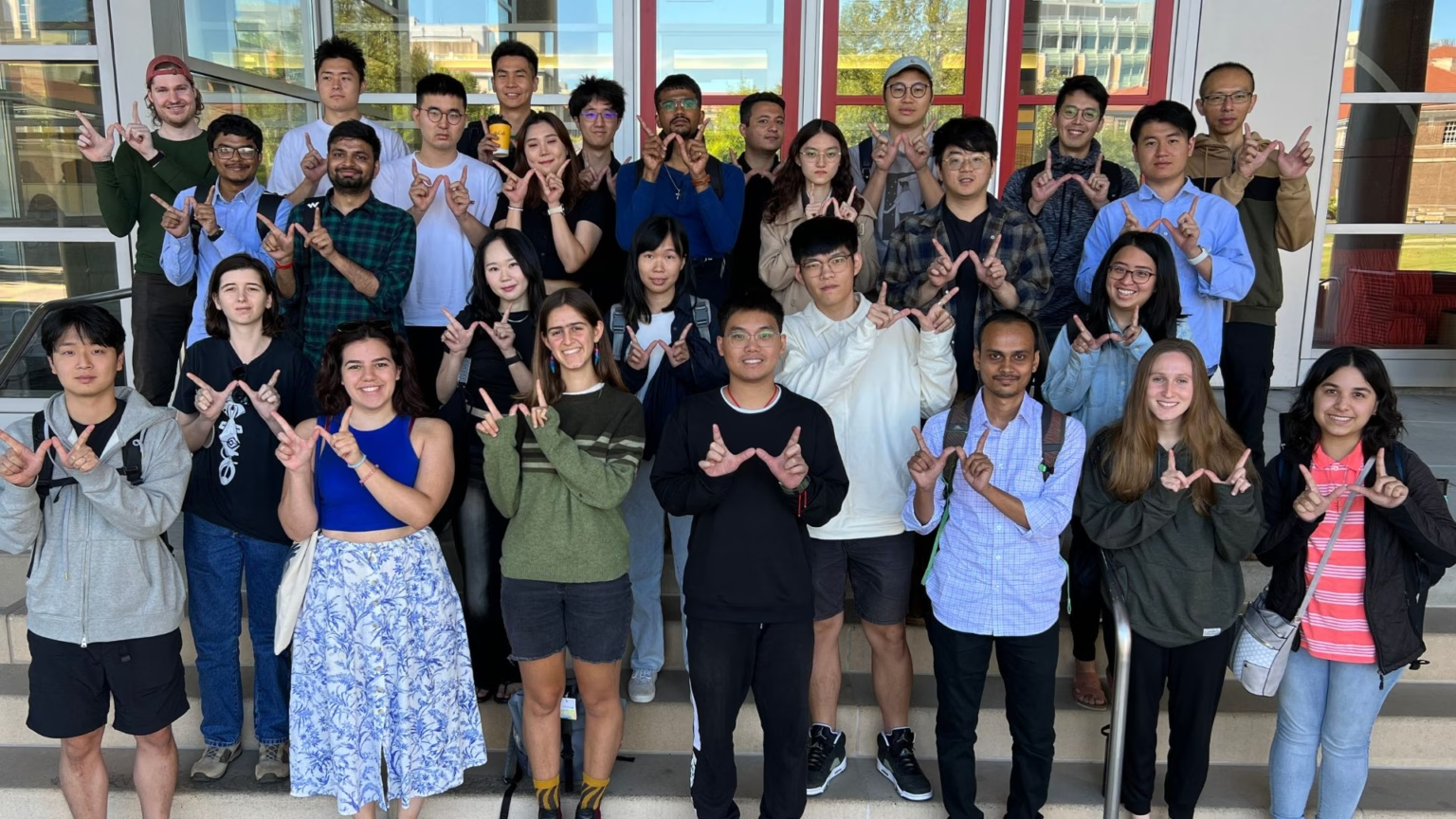 Students standing on steps in front of building making W shape with fingers